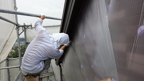 koushin_03kazusan | 外壁塗装は神奈川県横浜市の塗装職人 Worker in white hoodie on scaffolding, fastening plastic sheeting to the exterior wall.