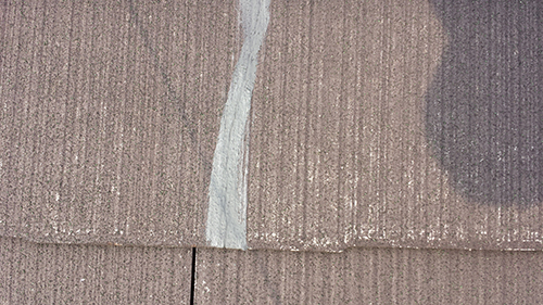 koushin_05clack | 外壁塗装は神奈川県横浜市の塗装職人 Close-up of brown roof shingles with a vertical gray sealant line along a seam.
