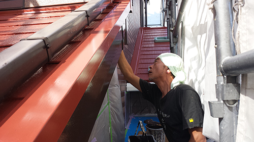 koushin_07hafu2 | 外壁塗装は神奈川県横浜市の塗装職人 Construction worker on scaffolding applying sealant along the edge of a red metal roof.