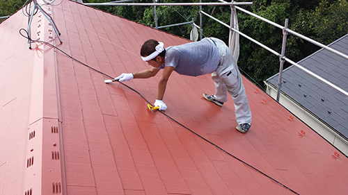 koushin_10engiri1 | 外壁塗装は神奈川県横浜市の塗装職人 Man on a red metal roof with safety rope, wearing gloves and a headband, wiping the surface with a cloth