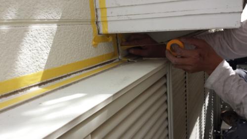 Person applying yellow painter's tape along a window frame on an exterior wall, preparing to paint.