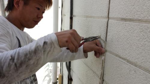 Person wearing a light sweatshirt chisels a concrete exterior wall with a metal tool held against the surface
