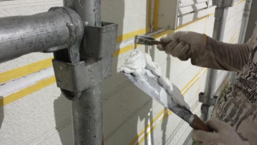 Worker on scaffolding smoothing caulk along an exterior wall with a rag-wrapped trowel.
