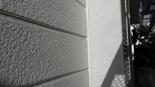 Exterior wall of a building with textured horizontal siding and a diagonal shadow on a white panel near the edge of a doorway or balcony area.