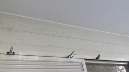Low-angle view of a light-colored ceiling with a metal curtain track and a few roller hooks along the top of a window underneath.