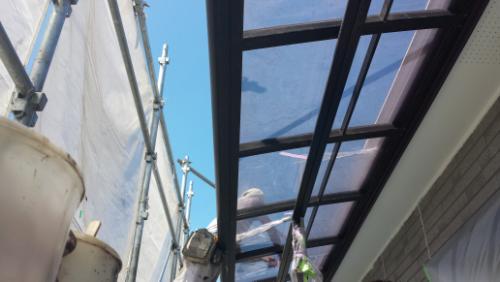 Scaffolding along an exterior wall with a glass roof panel over a walkway during construction; blue sky in the background.
