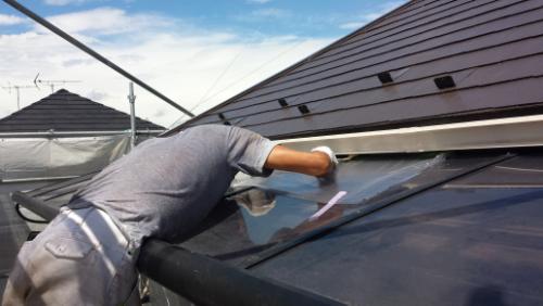 Worker on a sloped roof wiping a glass skylight with a cloth.